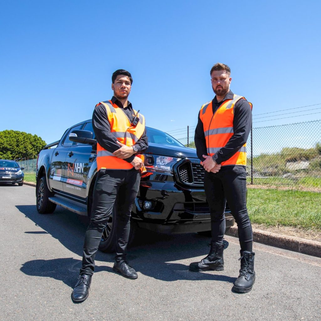 Two security guards in high-vis in front of an NHN vehicle