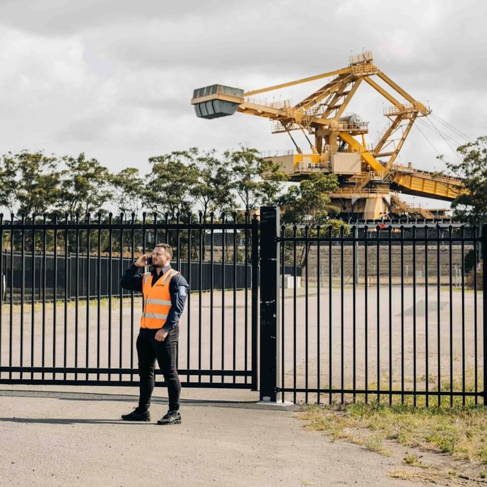 NHN employee taking a phone call in front of a gated industrial premises